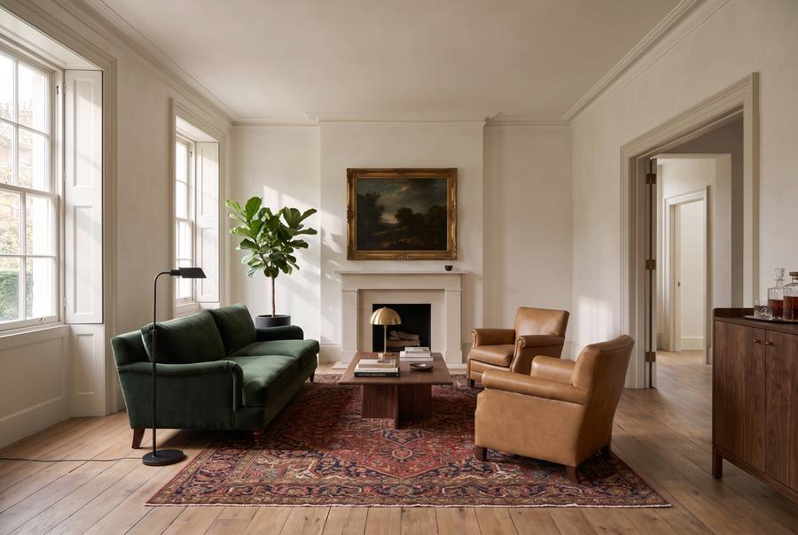 The same room restyled: a forest-green velvet sofa, tan leather club chairs, a Persian rug, a gilt-framed landscape.